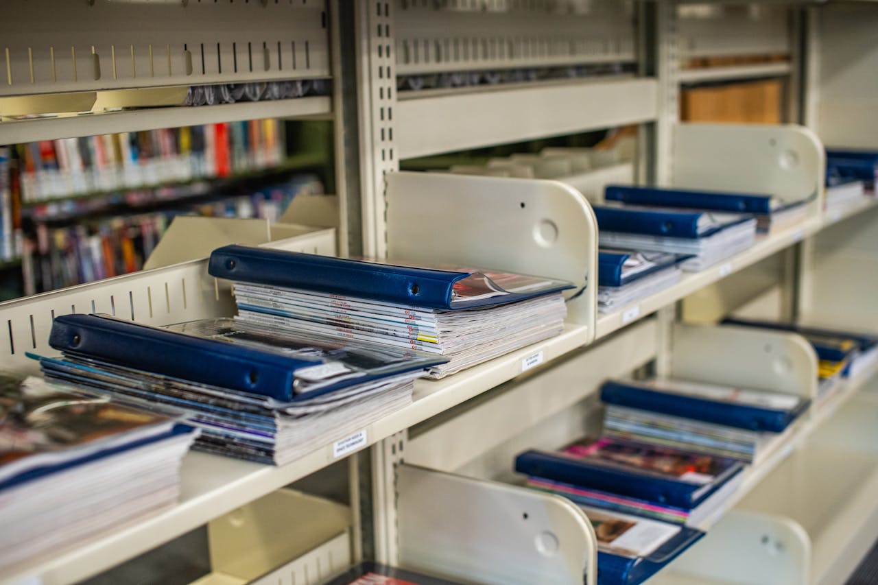 Neatly arranged binders and magazines on library shelves showcasing organization.
